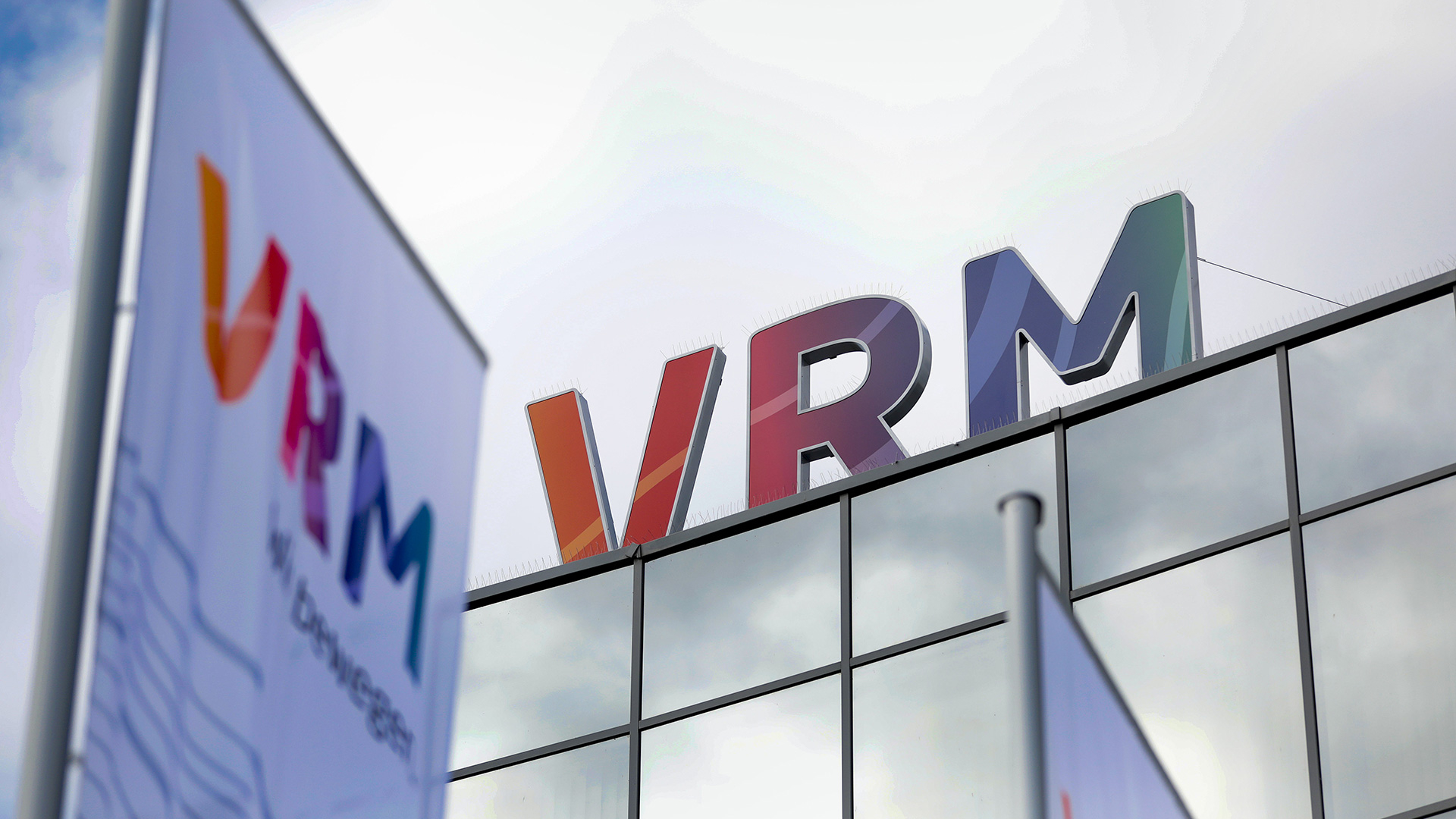 Das Logo der VRM ist auf dem Dach des Gebäudes und auf einer Fahne im Vordergrund zu sehen.