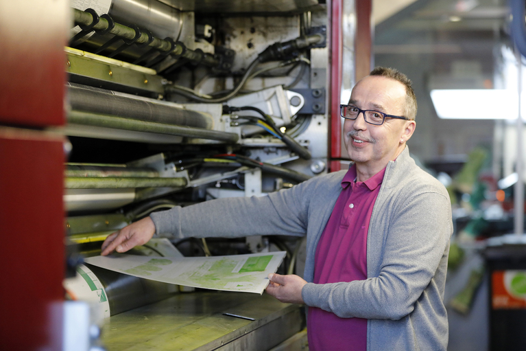 Ein freundlicher Mitarbeiter, der aus einer Druckerpresse die Zeitung holt.
